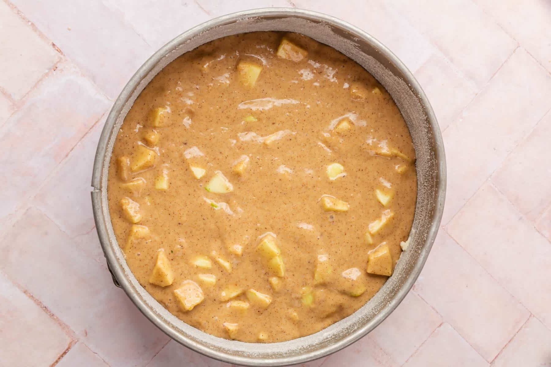 Gluten-free apple cake batter with diced apples in a springform pan before baking.