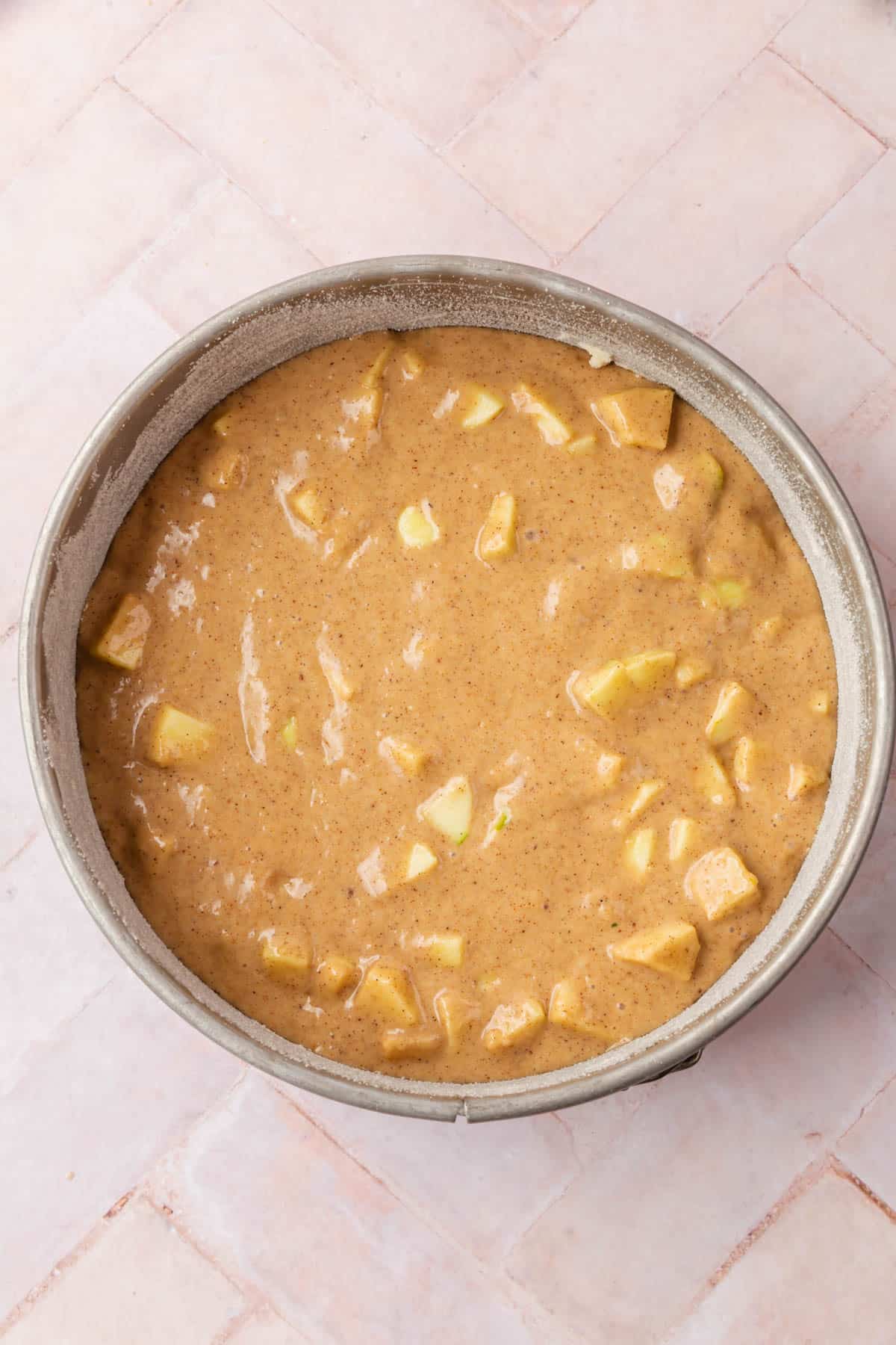 Gluten-free apple cake batter with diced apples in a springform pan before baking.