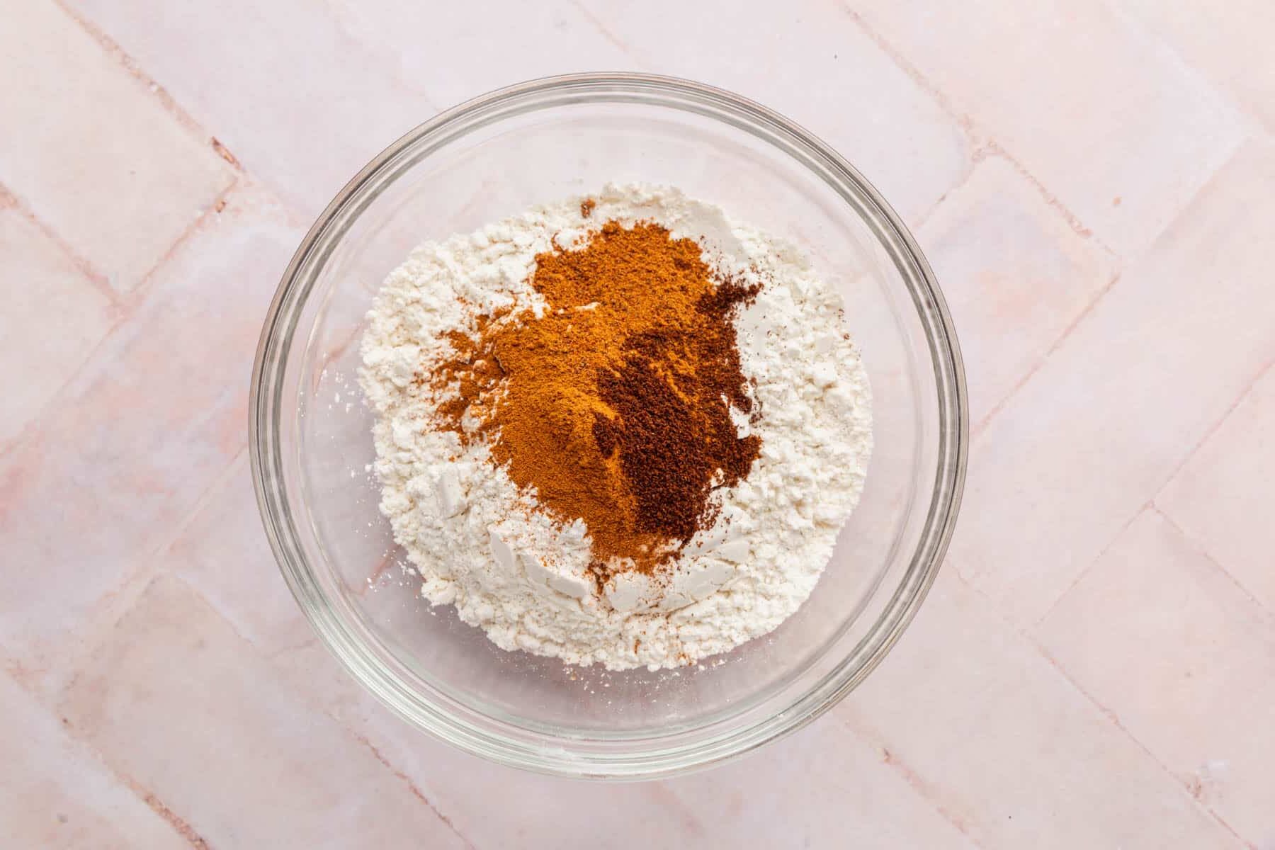A glass mixing bowl with gluten-free flour blend, baking soda, baking powder, salt, cinnamon, nutmeg, and cloves before mixing.