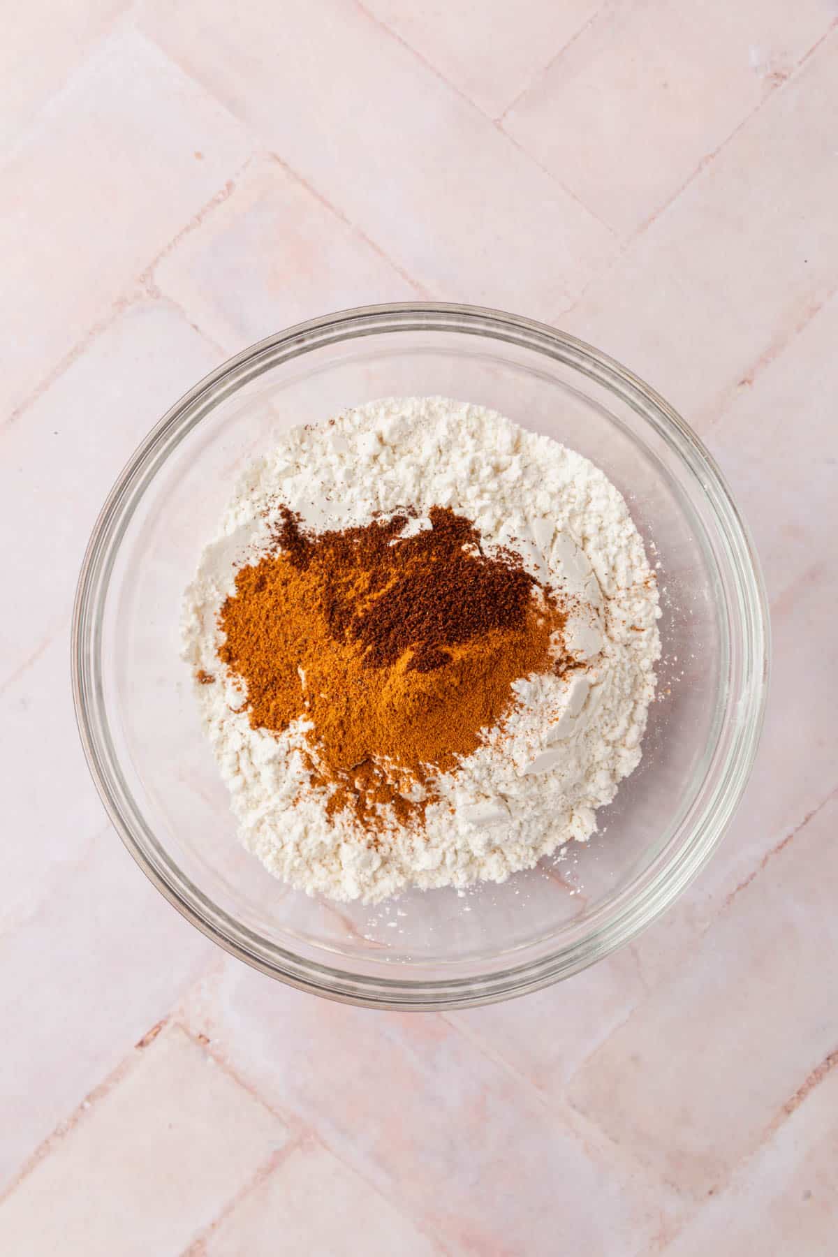 A glass mixing bowl with gluten-free flour blend, baking soda, baking powder, salt, cinnamon, nutmeg, and cloves before mixing.