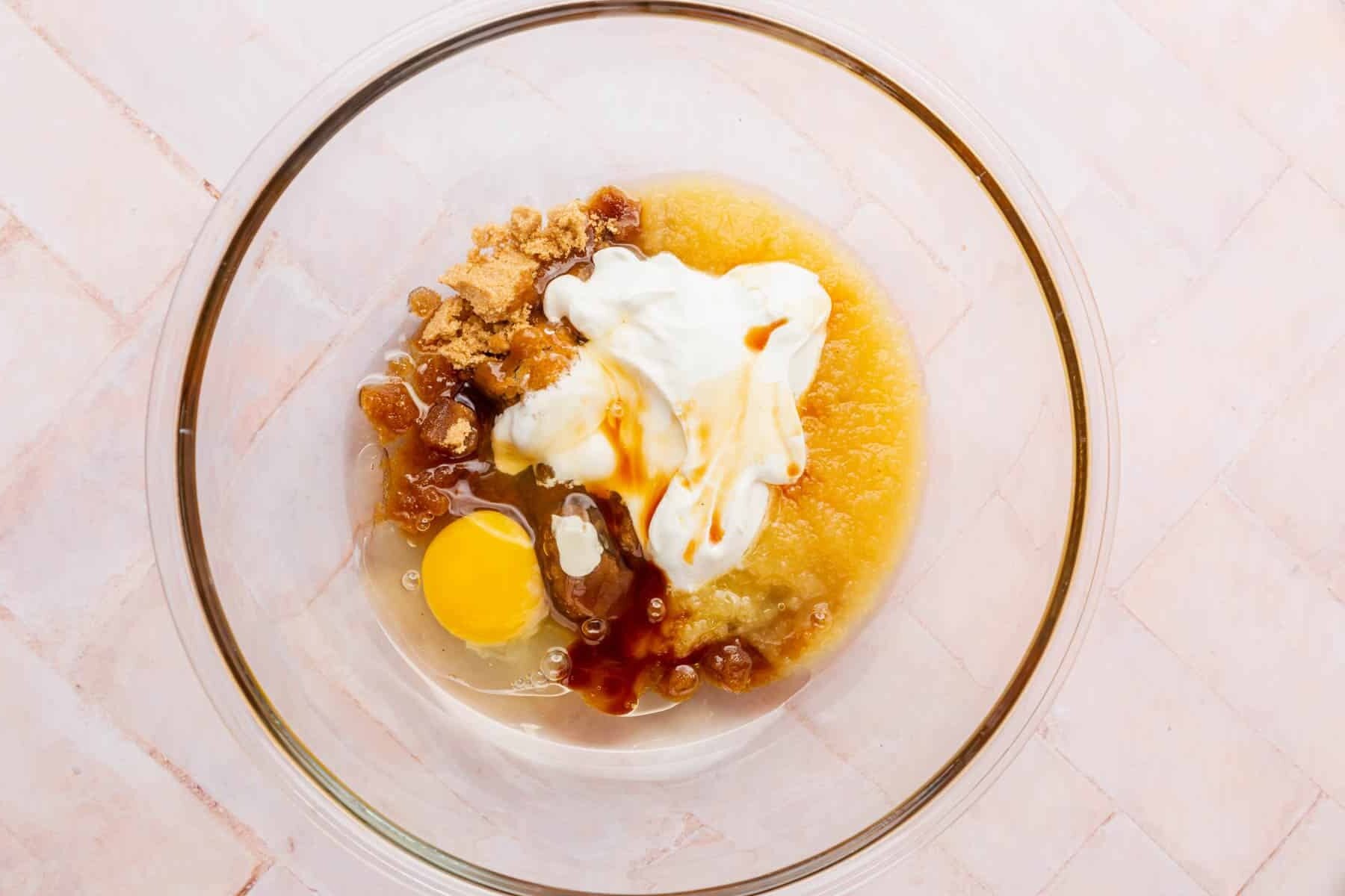 A glass mixing bowl with oil, brown sugar, eggs, sour cream, applesauce, and vanilla before mixing.