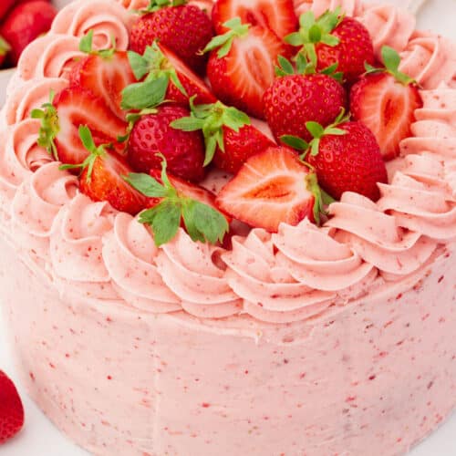 A whole uncut gluten-free strawberry cake frosted with strawberry buttercream piping and halved strawberries.