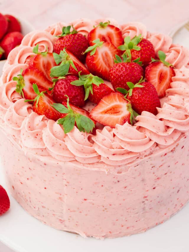 A whole uncut gluten-free strawberry cake frosted with strawberry buttercream piping and halved strawberries.
