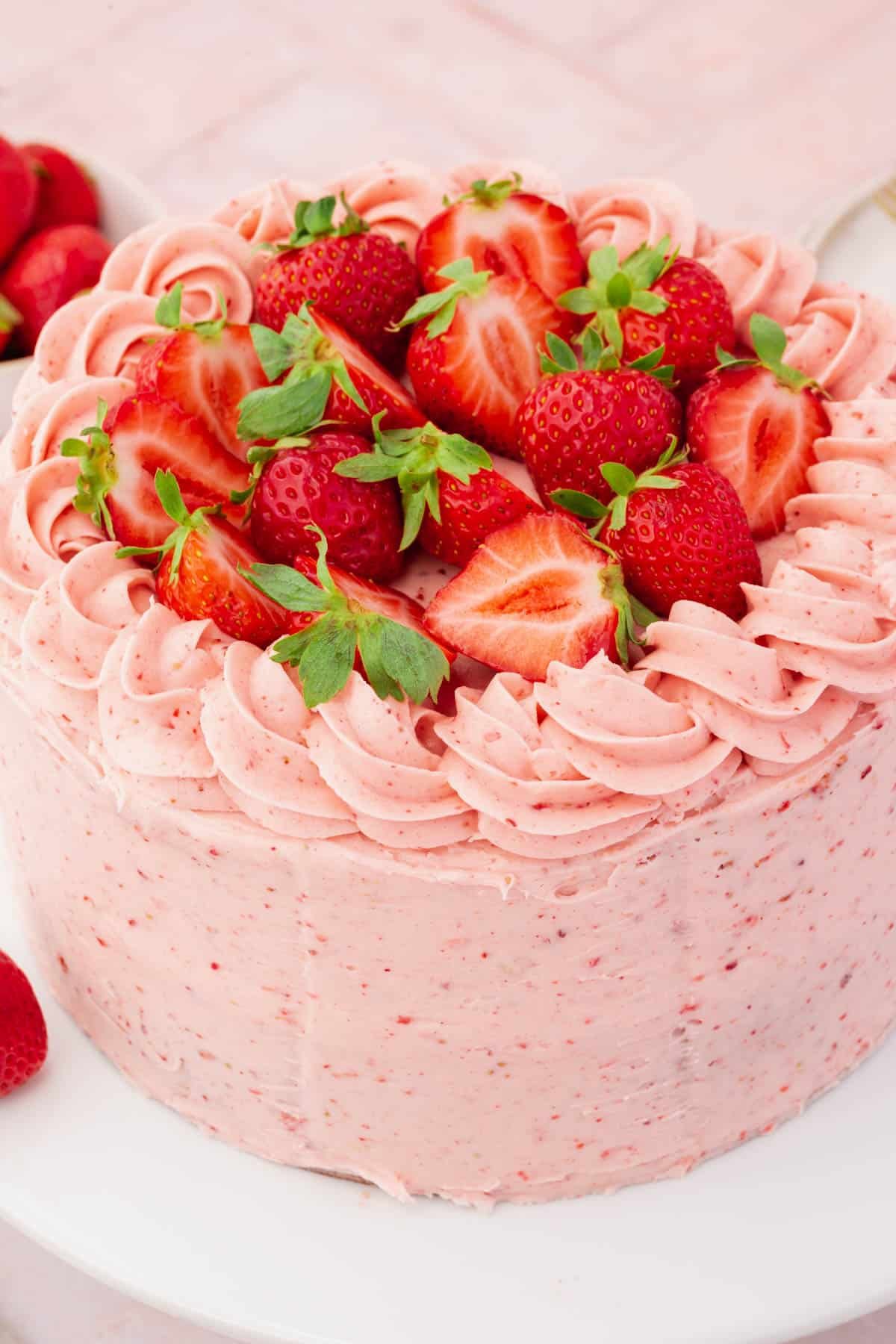 A whole uncut gluten-free strawberry cake frosted with strawberry buttercream piping and halved strawberries. 