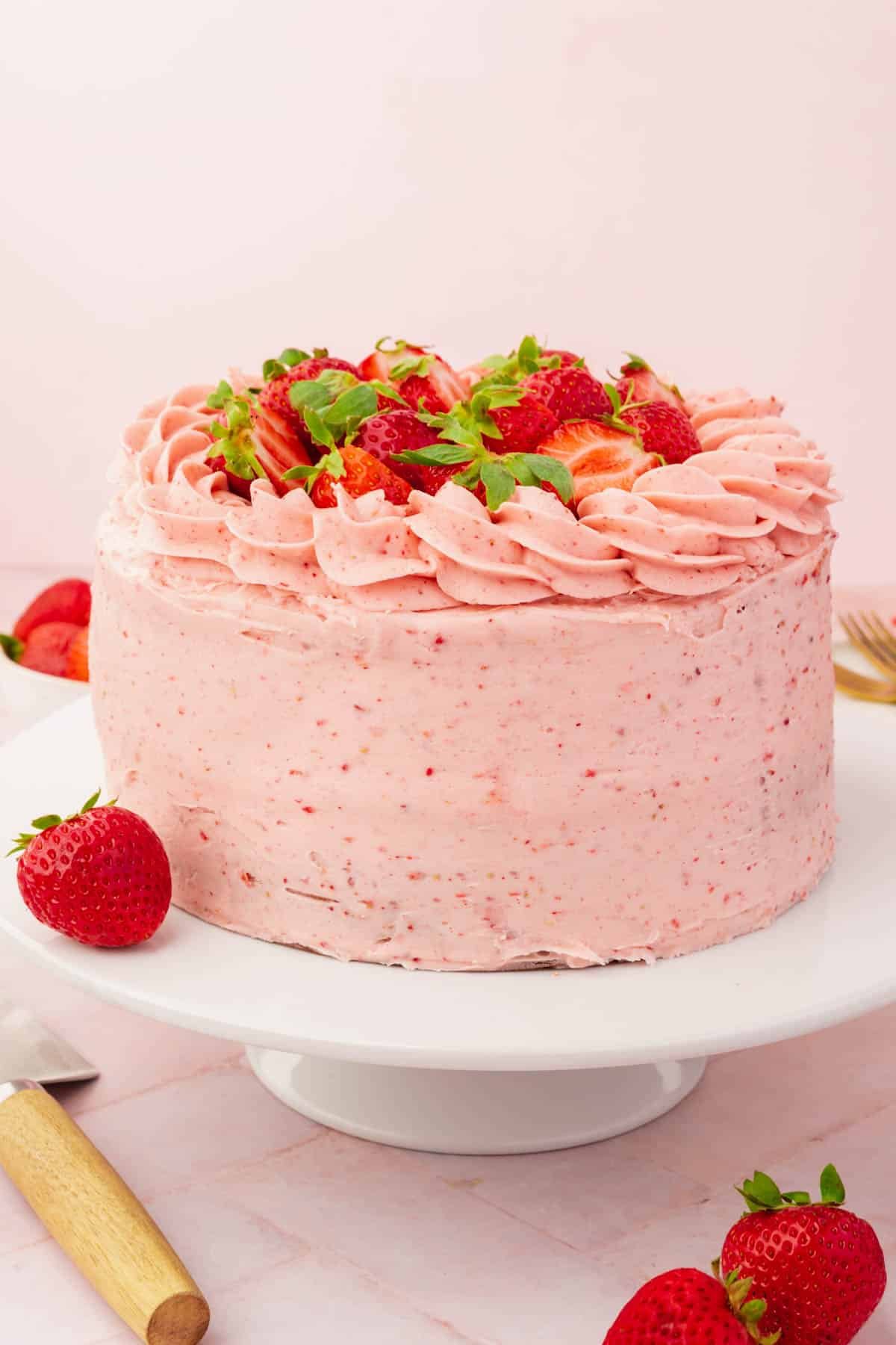 A whole gluten-free strawberry cake on a white cake stand on a pink table.