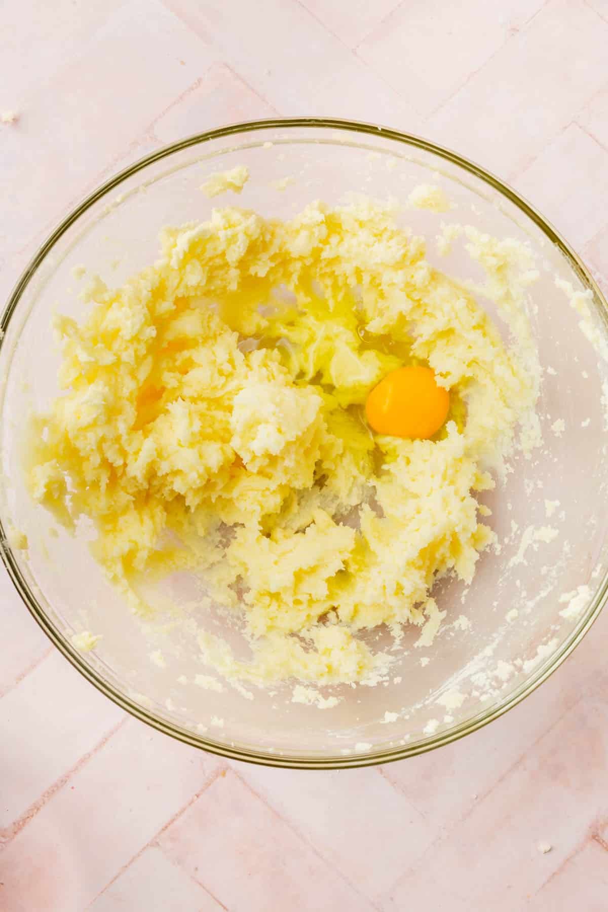 A glass mixing bowl with a creamed butter and sugar mixture topped with an egg.