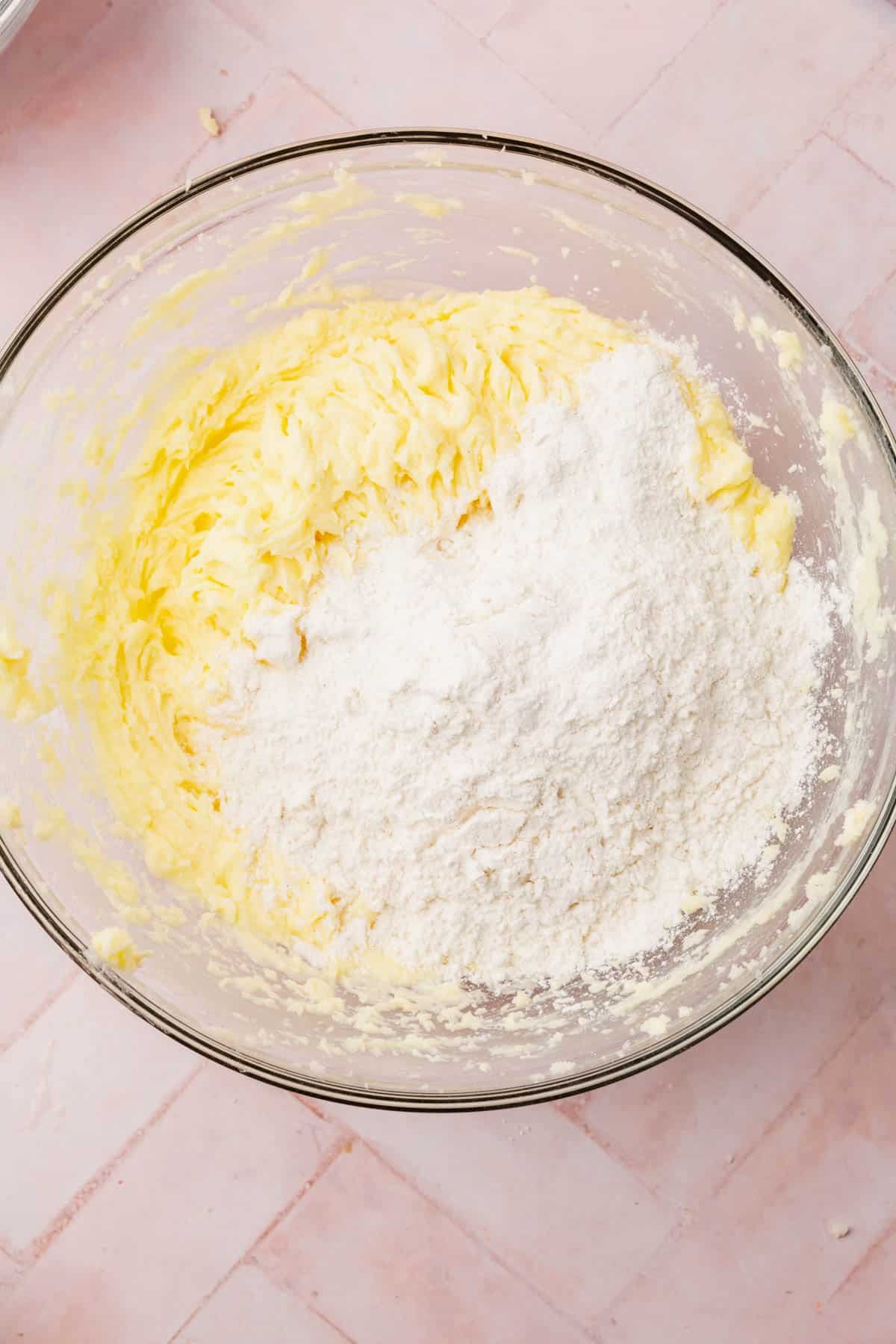 A glass mixing bowl with a creamed butter and sugar mixture topped with gluten-free flour blend.