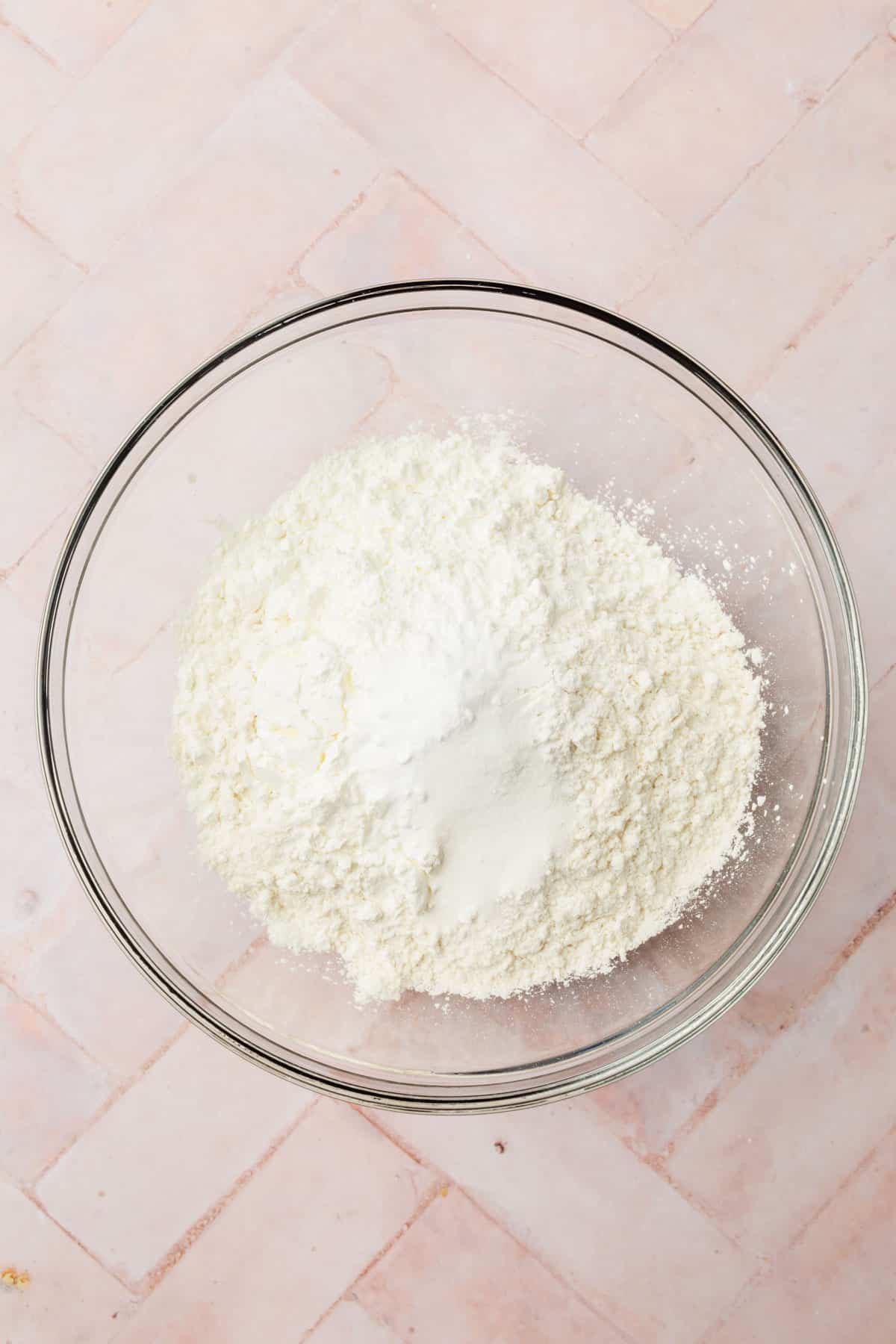 A glass mixing bowl with gluten-free flour blend, cornstarch, salt, baking powder, and baking soda in it before mixing.