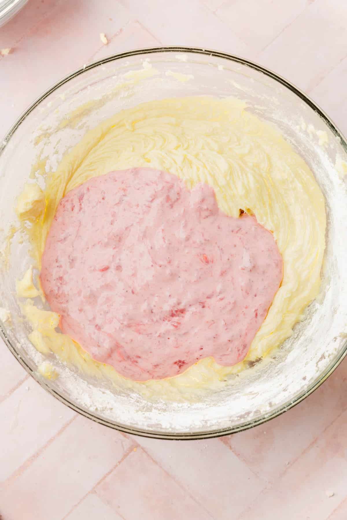 A vanilla cake batter in a mixing bowl topped with a strawberry sour cream mixture.