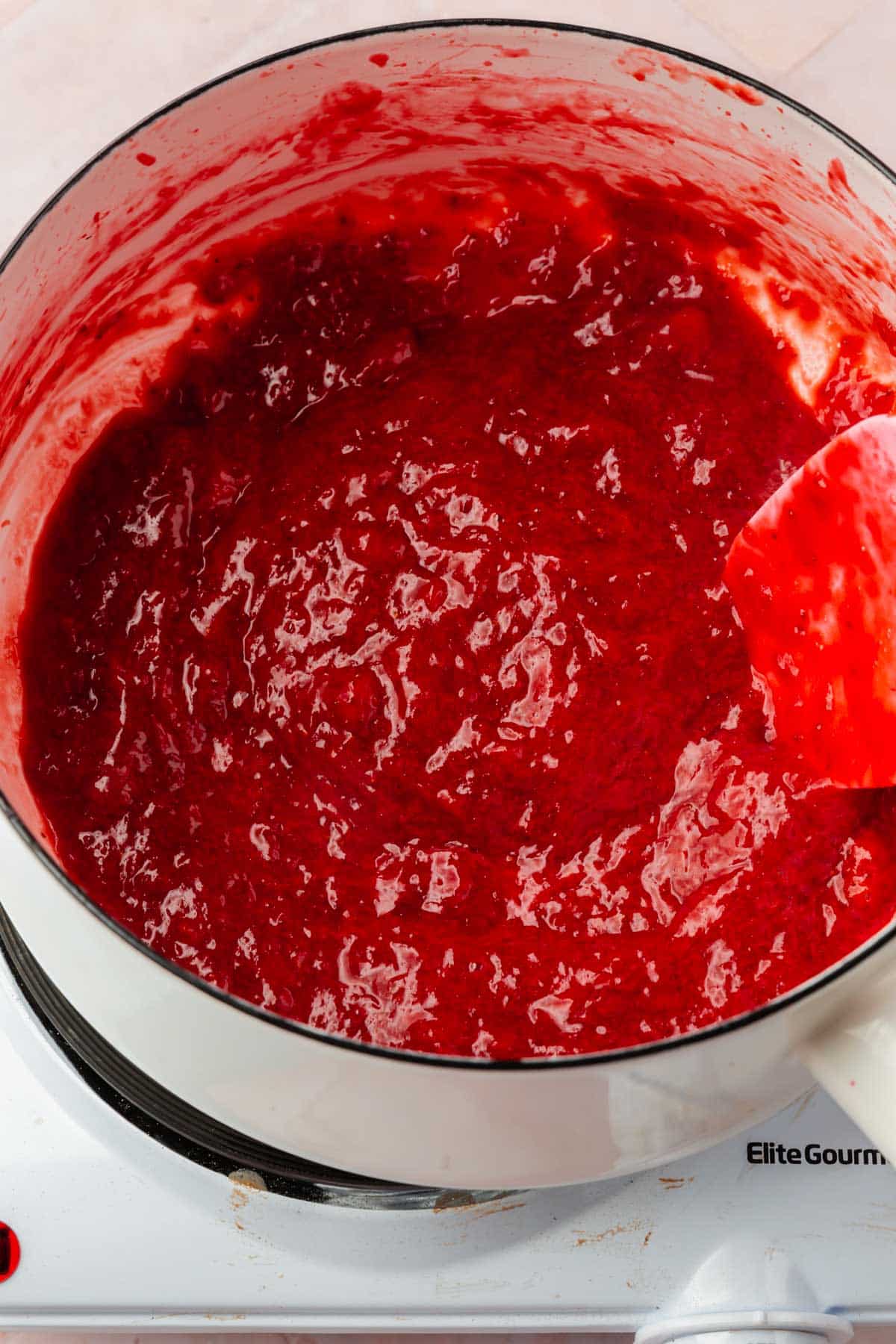 A white saucepan with a pureed strawberry reduction in it.