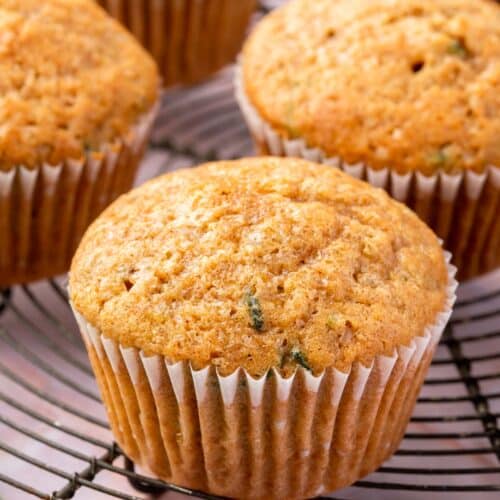 A closeup of a gluten-free zucchini muffin on a round cooling rack with more muffins in the backgroudn.