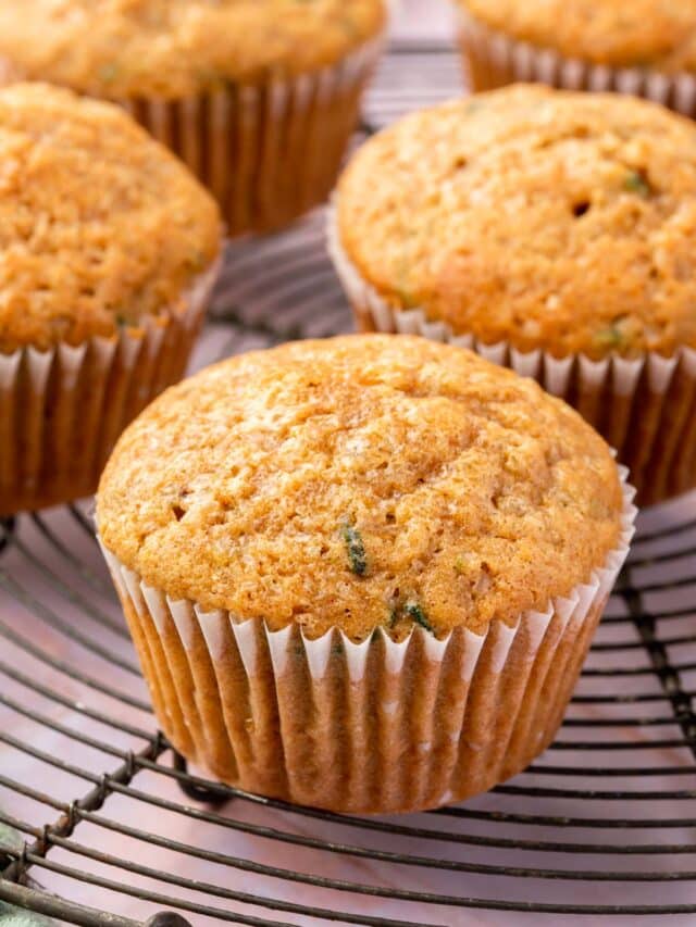 A closeup of a gluten-free zucchini muffin on a round cooling rack with more muffins in the backgroudn.