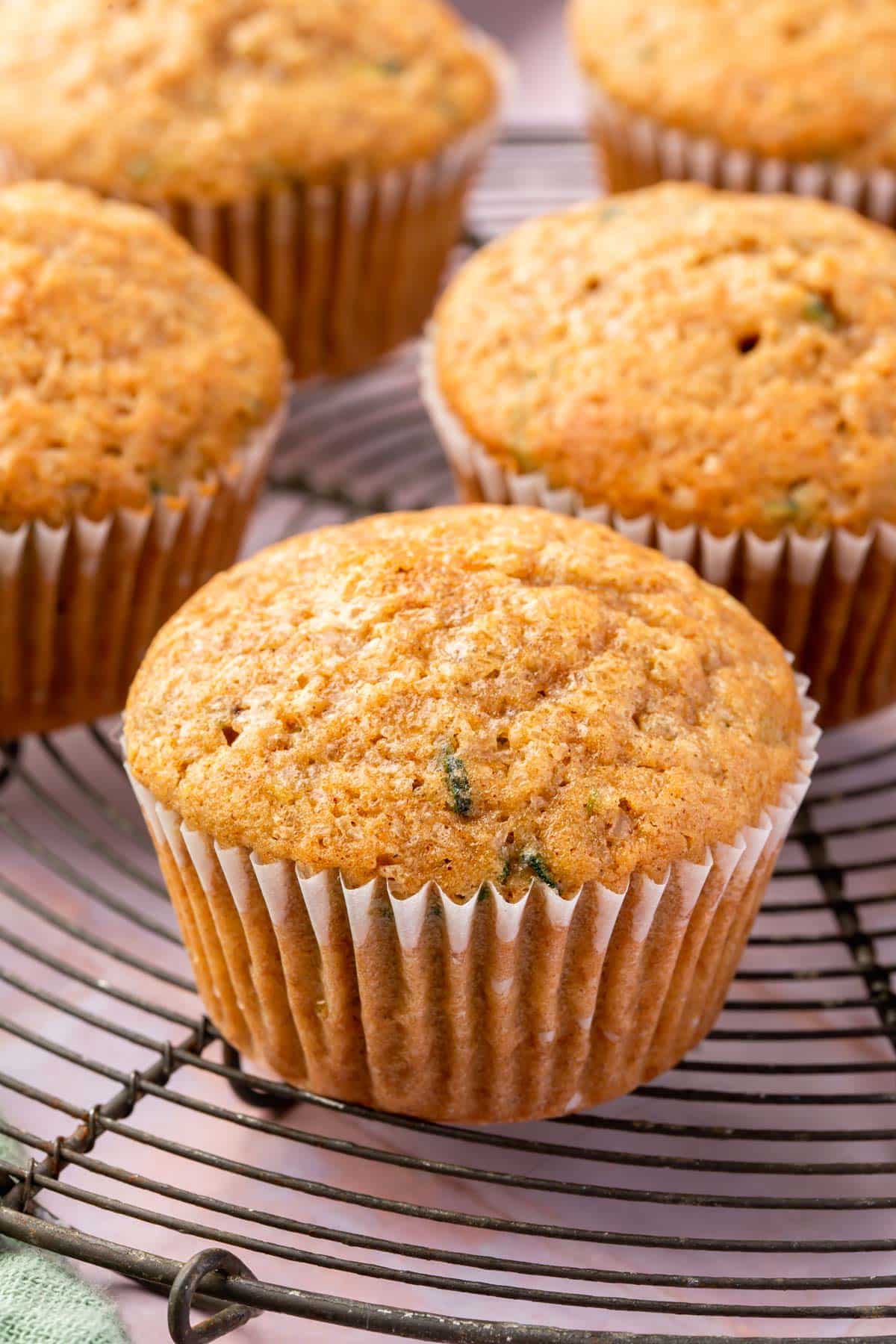 A closeup of a gluten-free zucchini muffin on a round cooling rack with more muffins in the backgroudn.
