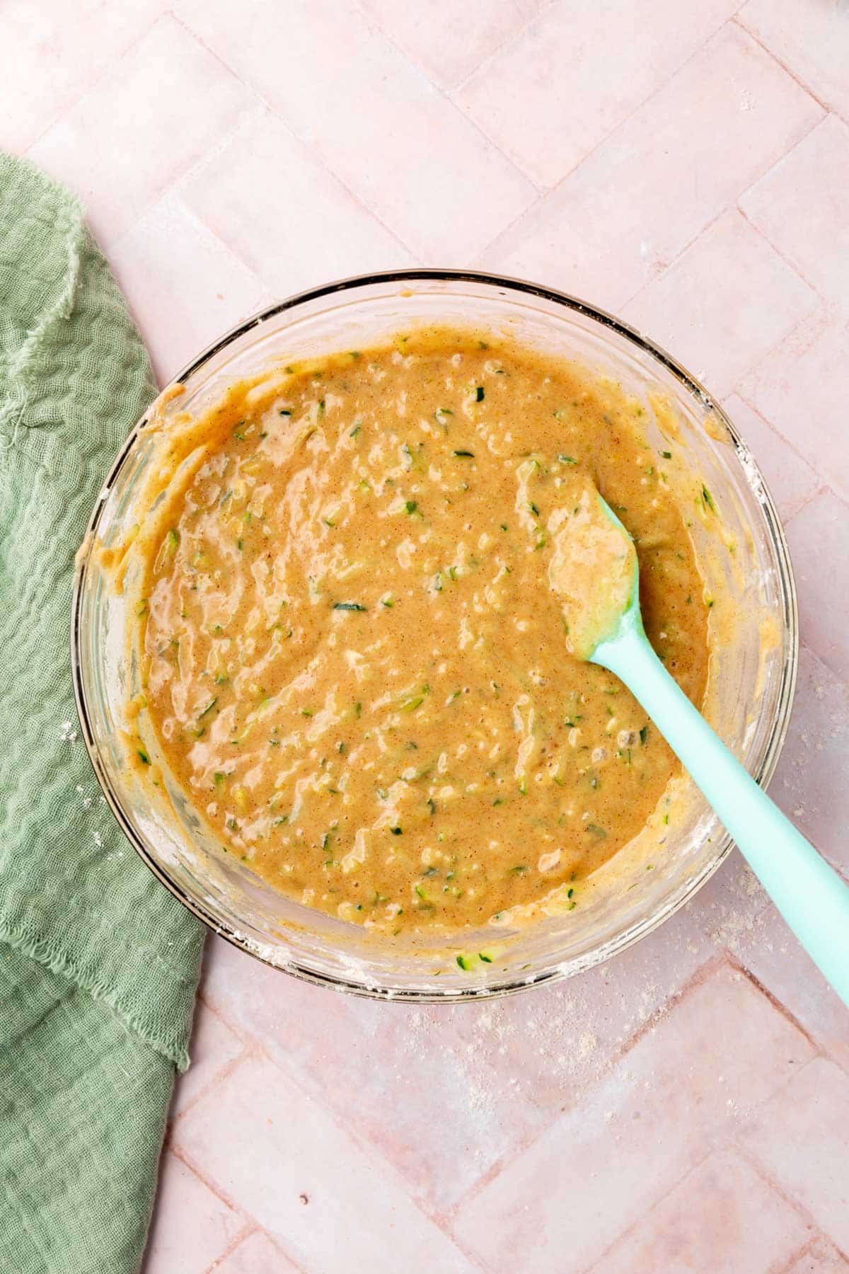 A bowl of gluten-free zucchini muffin batter with a blue spatula.