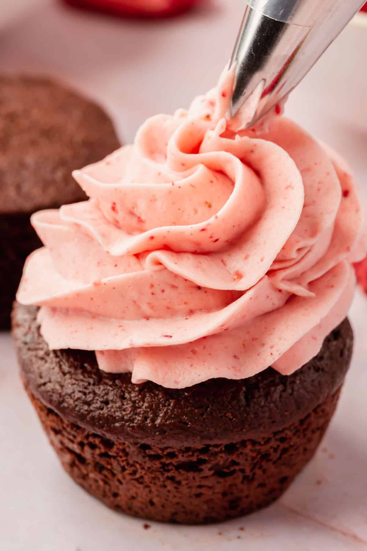 Strawberry frosting in the process of being piped on top of a chocolate cupcake.