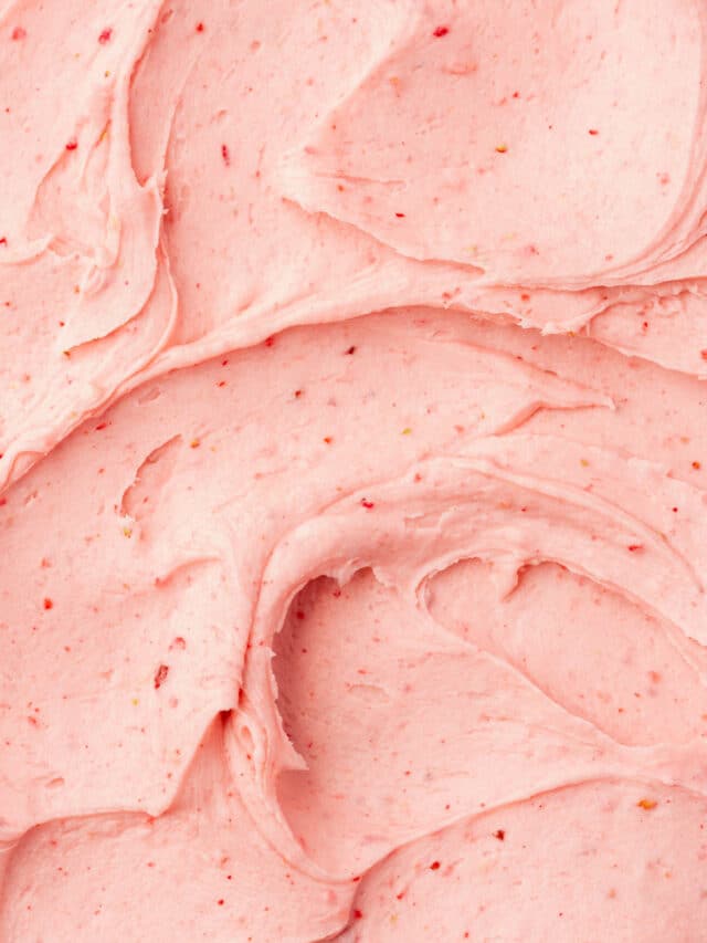 A closeup of swooshes of creamy strawberry frosting that has topped a cake and fills the whole frame.