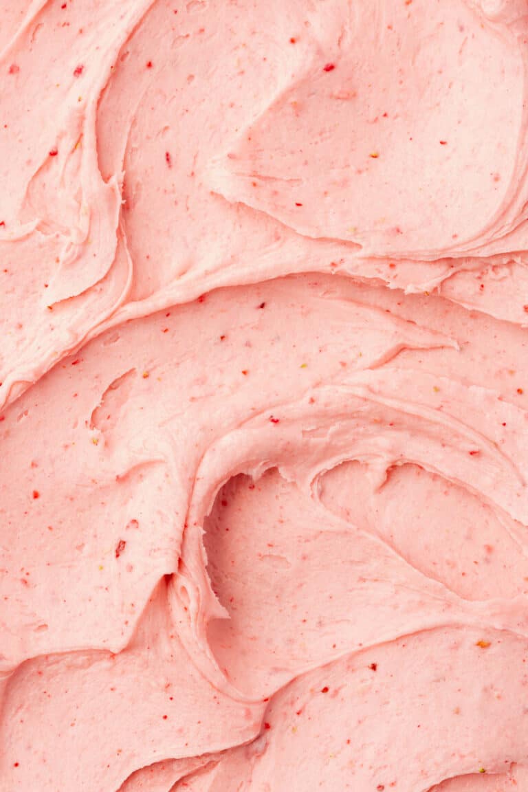 A closeup of swooshes of creamy strawberry frosting that has topped a cake and fills the whole frame.