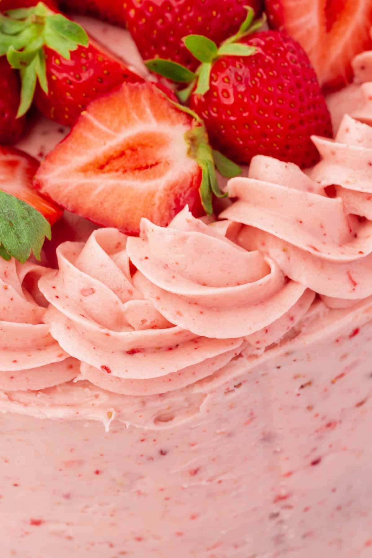 A close up of piped and frosted strawberry buttercream on a cake topped with fresh strawberry havles.