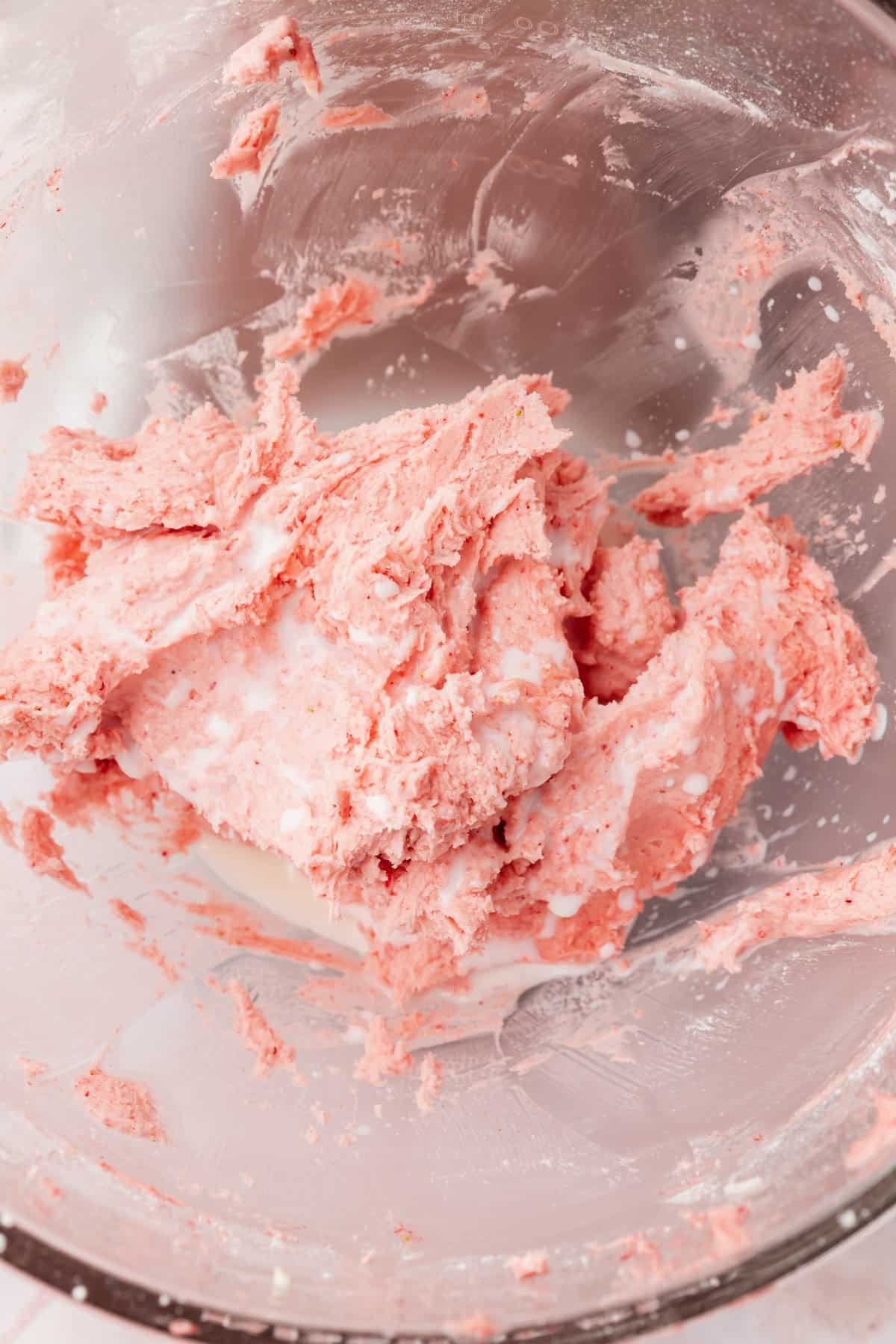 Mixed strawberry buttercream topped with whole milk before mixing in the bowl of a stand mixer.