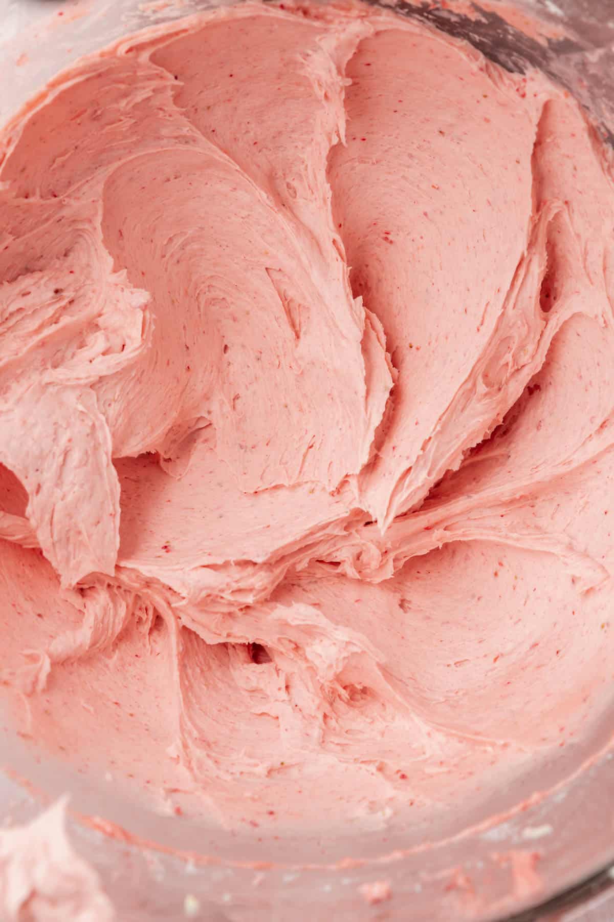 Creamy strawberry frosting that has been mixed in the bowl of a stand mixer.