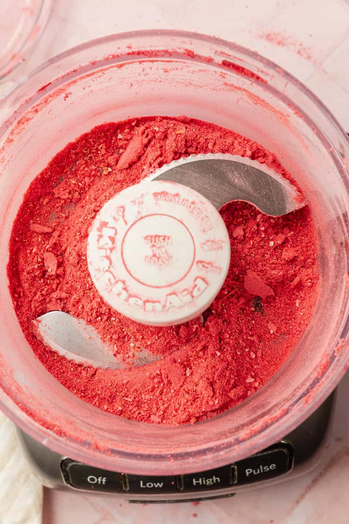 A food processor with freeze-dried strawberries in it that have been pulverized to a powder.