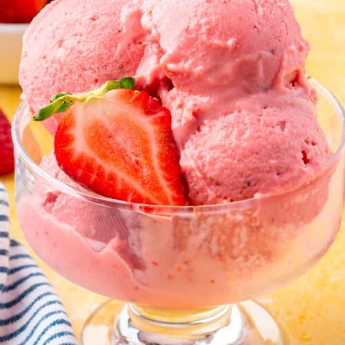 A close up of scoops of strawberry frozen yogurt in a glass bowl with slices of fresh strawberries on top.