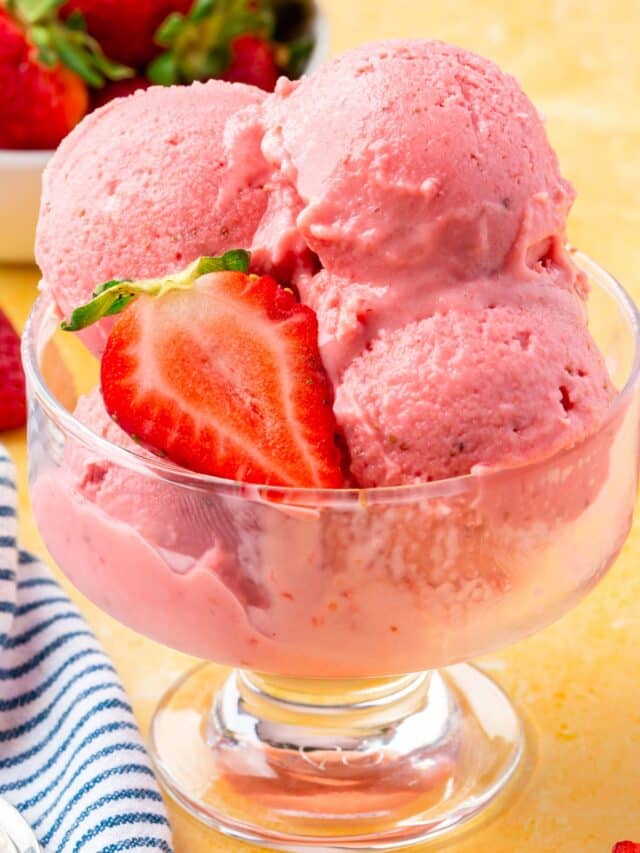 A close up of scoops of strawberry frozen yogurt in a glass bowl with slices of fresh strawberries on top.