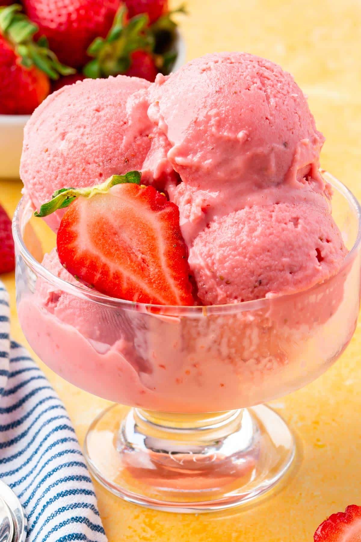 A close up of scoops of strawberry frozen yogurt in a glass bowl with slices of fresh strawberries on top.