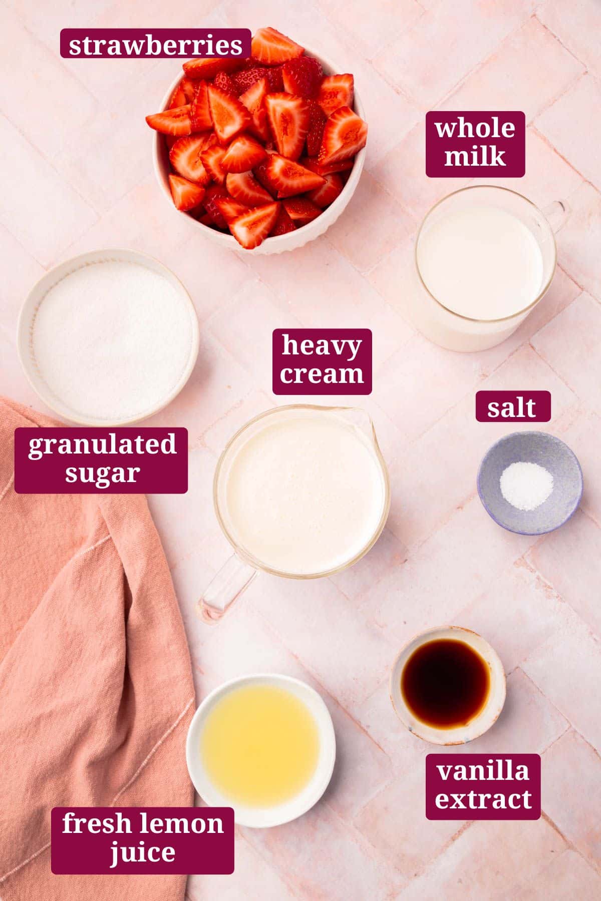 Small bowls on a pink herringbone table for making strawberry ice cream, including strawberries, milk, heavy cream, sugar, vanilla, lemon juice, and salt with text overlays over each ingredient.