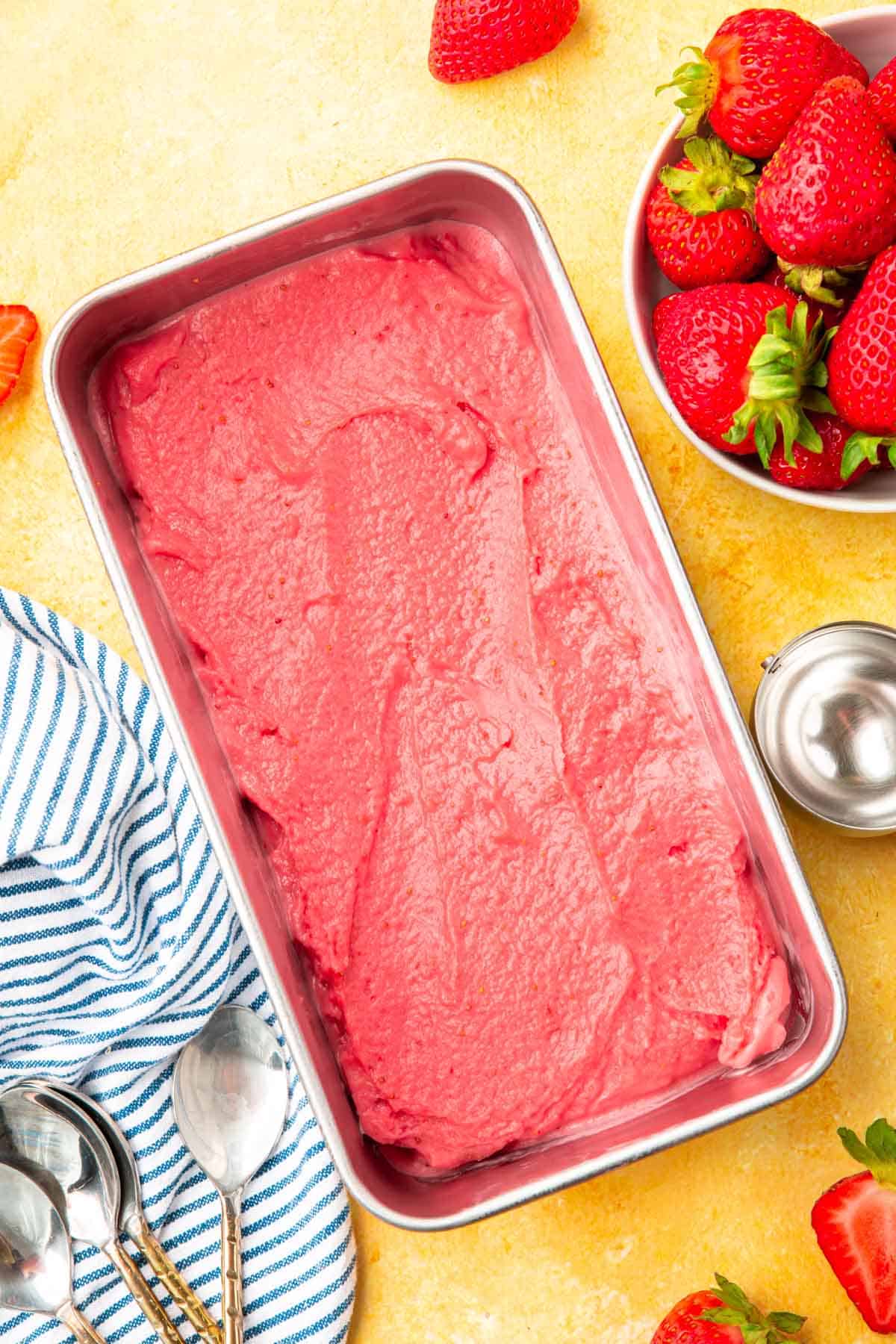 A loaf pan with strawberry frozen yogurt in it with a bowl of strawberries to the side.