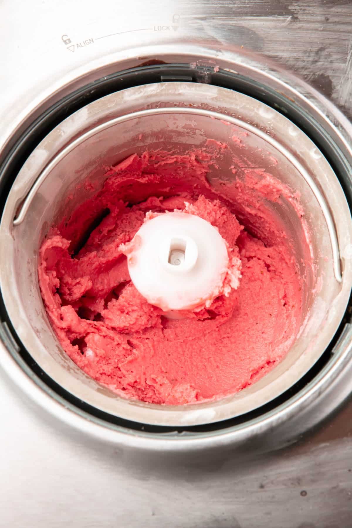 An ice cream maker with strawberry frozen yogurt in it after churning.