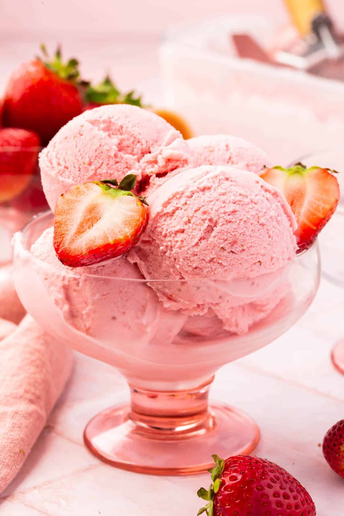 A pink footed bowl with scoops of strawberry ice cream topped with strawberry halves.