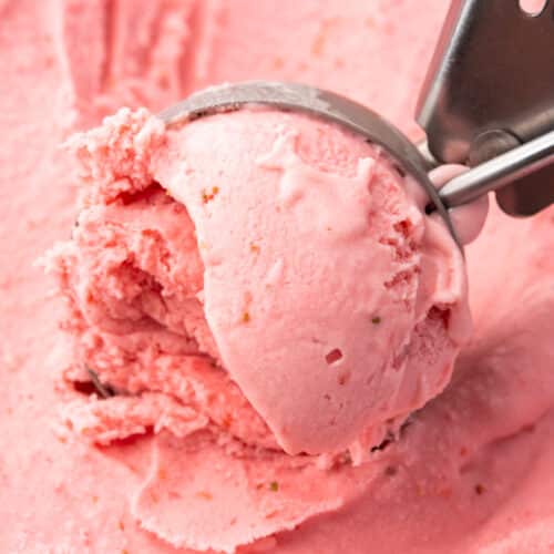 An ice cream scooper scooping strawberry ice cream from a tub.
