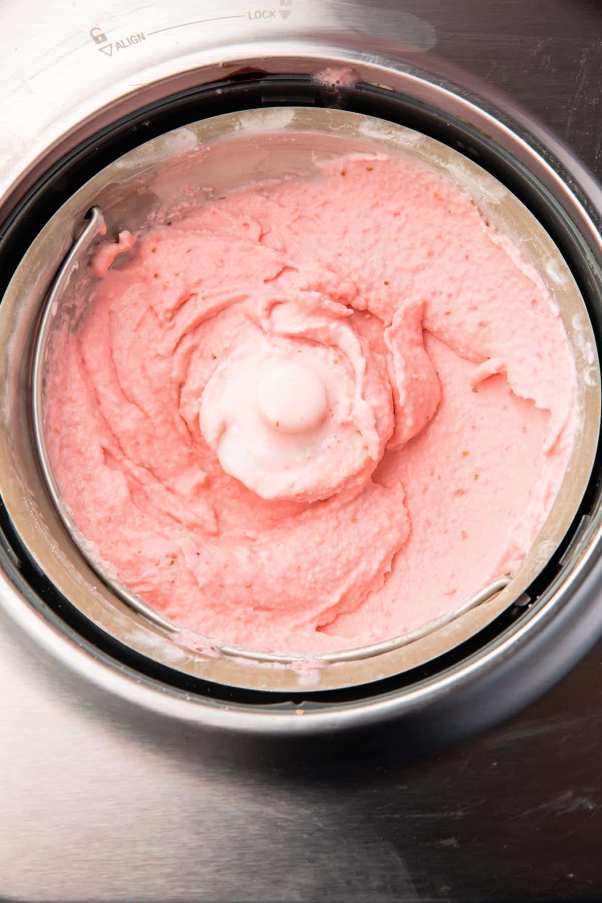An ice cream maker with churned strawberry ice cream in it.