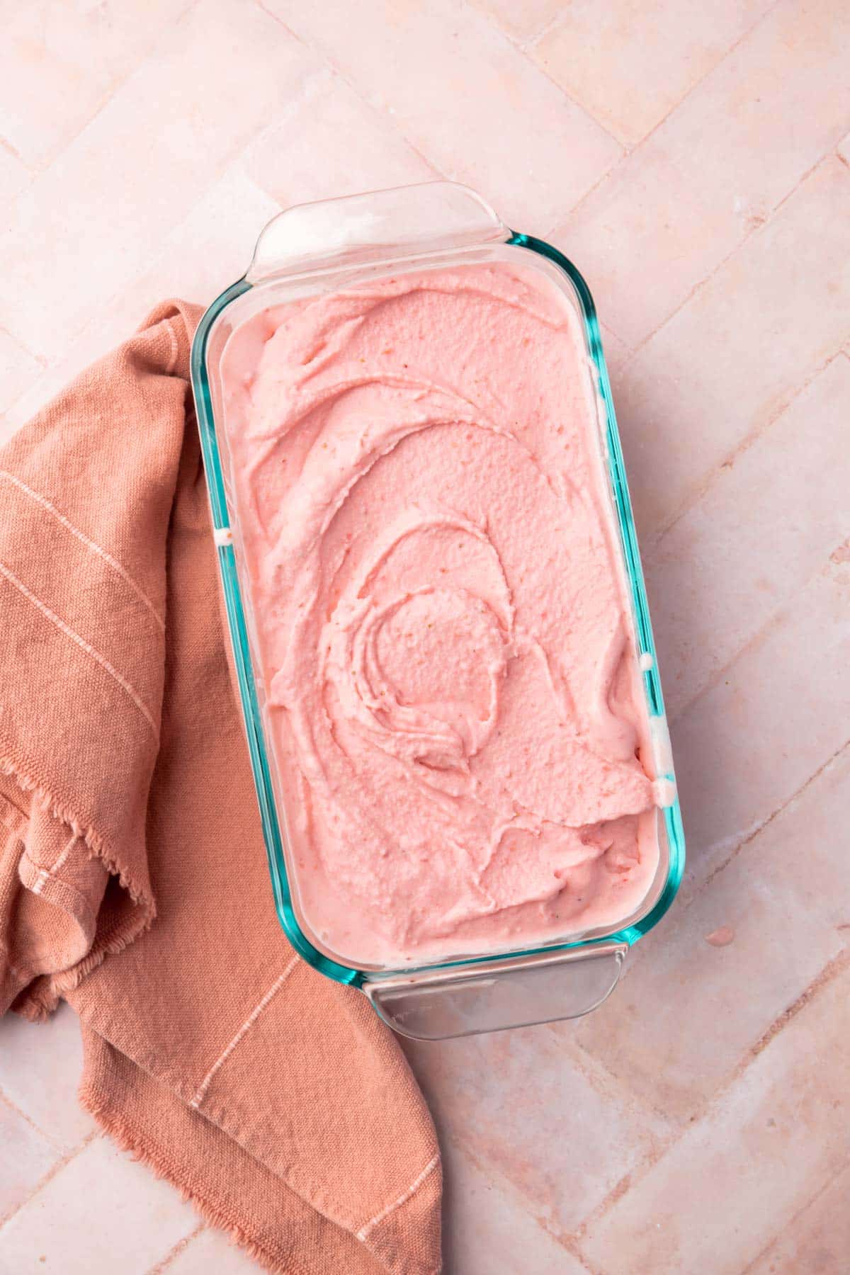 A glass loaf pan filled with strawberry ice cream on a pink herringbone table.
