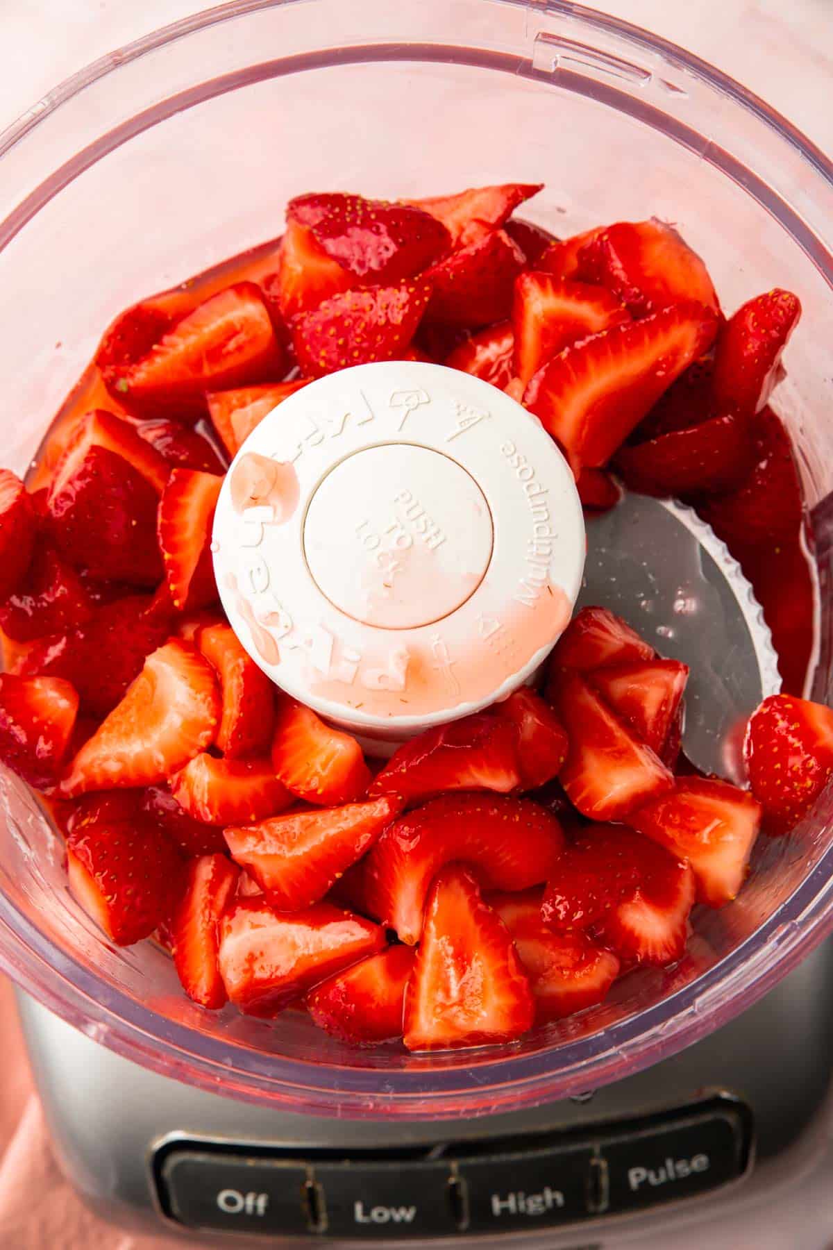 A food processor with sliced macerated strawberries in it.