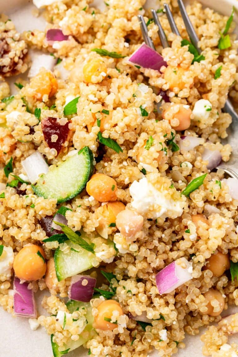 A closeup of quinoa chickpea salat topped with sliced cucumber, chopped red onion, feta, and fresh parsley.