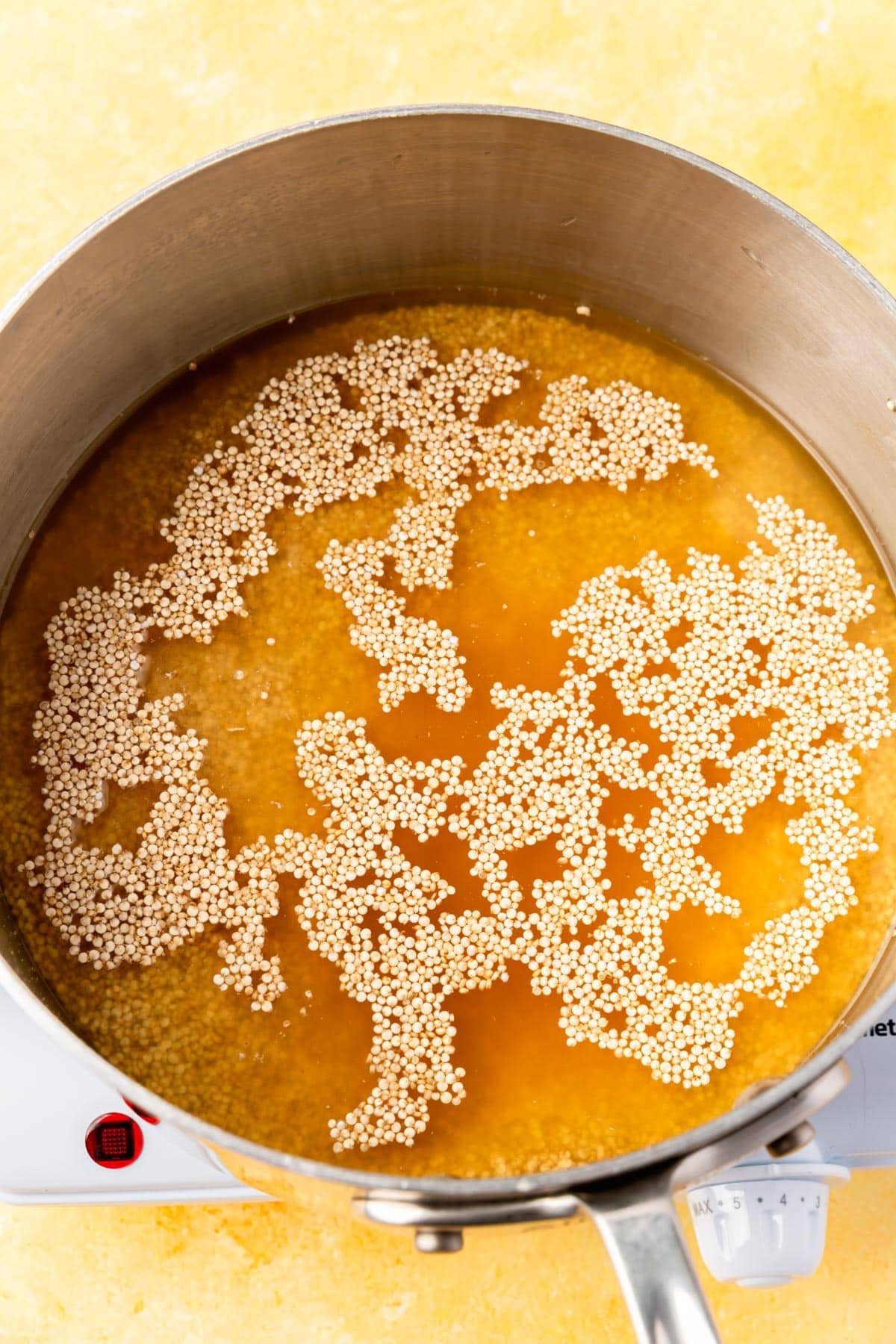 A saucepan with vegetable broth and uncooked quinoa before cooking.