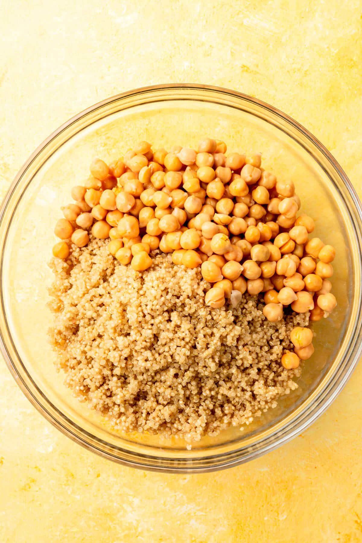 A glass mixing bowl with canned chickpeas and cooked quinoa in it before mixing together.