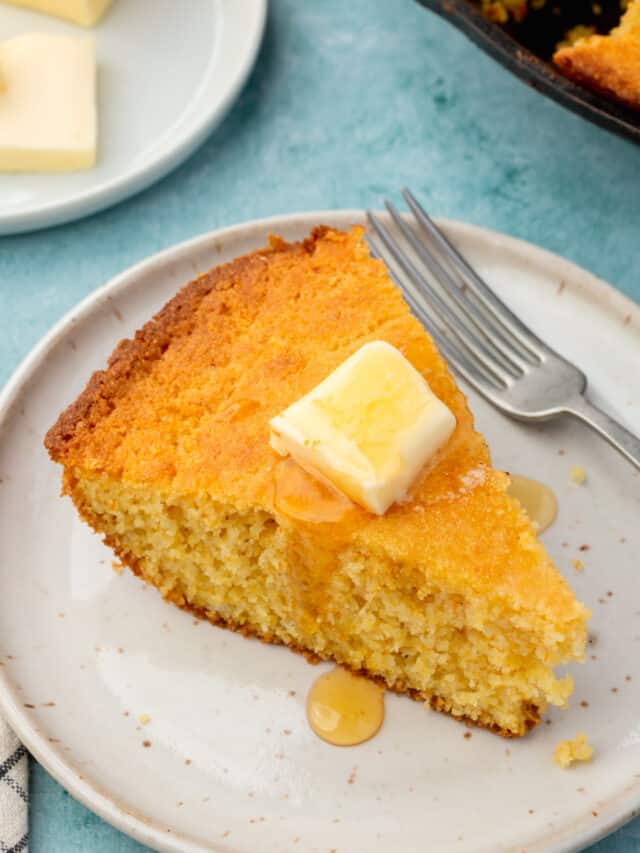 A wedge of gluten-free cornbread topped with melted butter and honey on an appetizer plate with a fork.