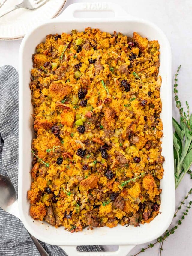 An overhead view of a rectangle casserole dish filled with gluten-free cornbread stuffing topped with fresh thyme, dried cranberries, and Italian sausage.