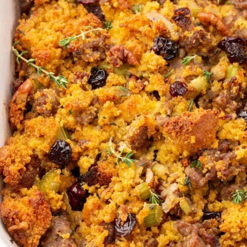 A closeup of a casserole dish with gluten-free cornbread sausage stopping topped with fresh thyme and dried cranberries.