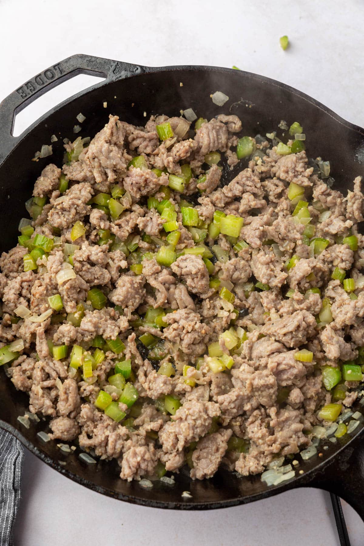Cooked Italian sausage, onions, and celery mixed together in a cast iron skillet.
