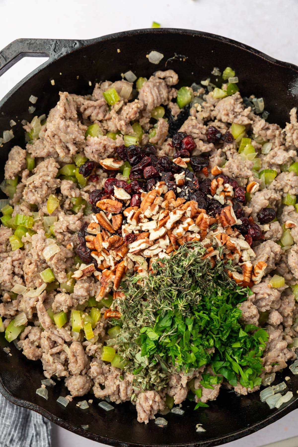 A cast iron skillet filled with Italian sausage, celery, onions, sage, thyme, pecans and cranberries before mixing together.