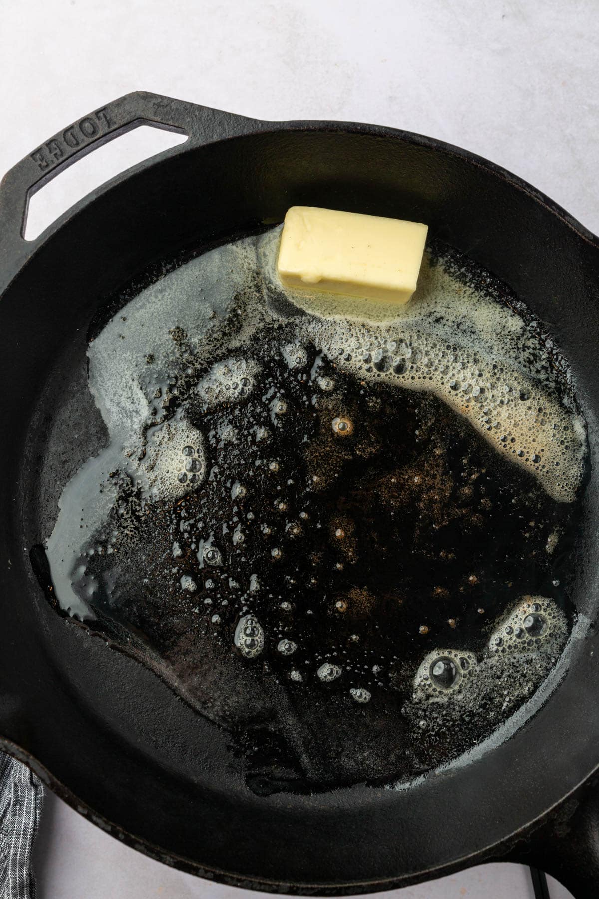 A cast iron skillet with a stick of butter that is starting to melt.