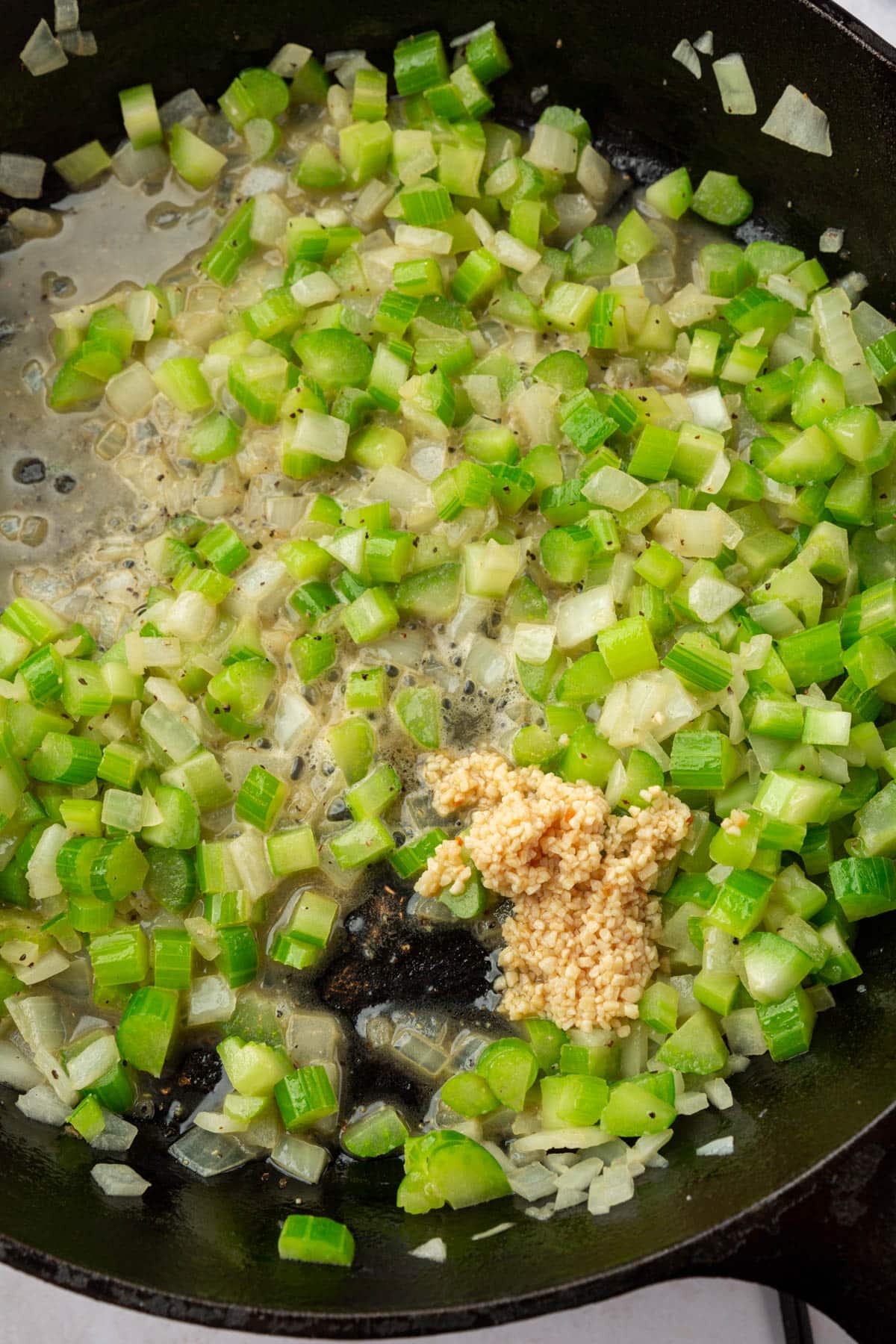 A cast iron skillet filled with sautéed onions and celery with minced garlic.