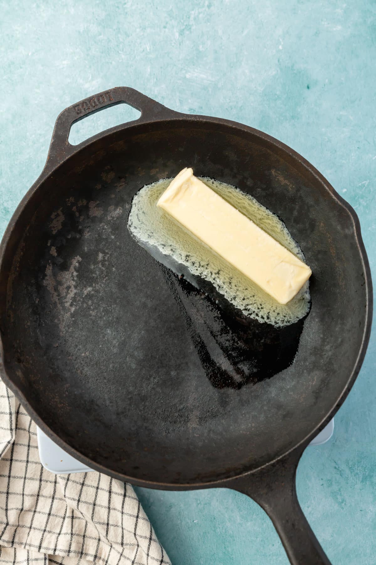 A cast iron skillet with a stick of butter in it that is starting to melt.