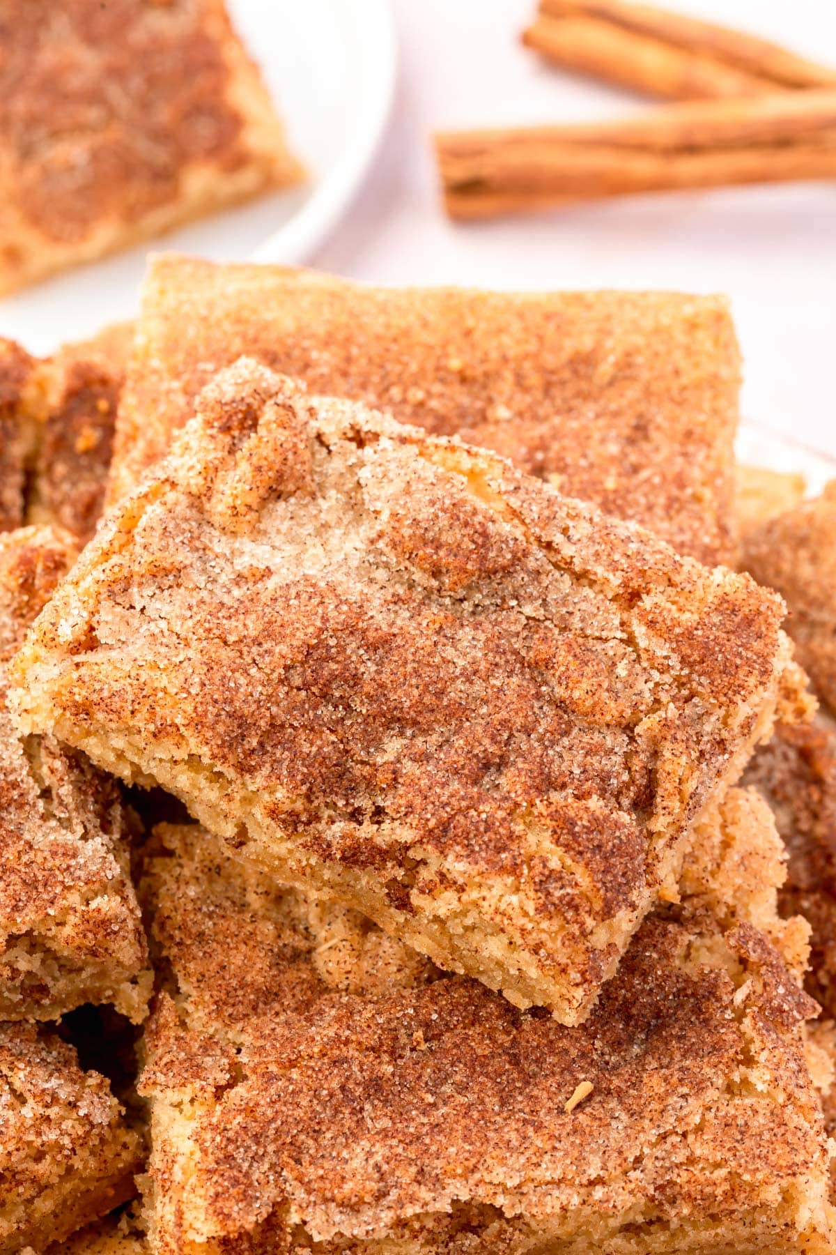 A stack of gluten-free snickerdoodle bars on a plate with cinnamon sticks in the background.