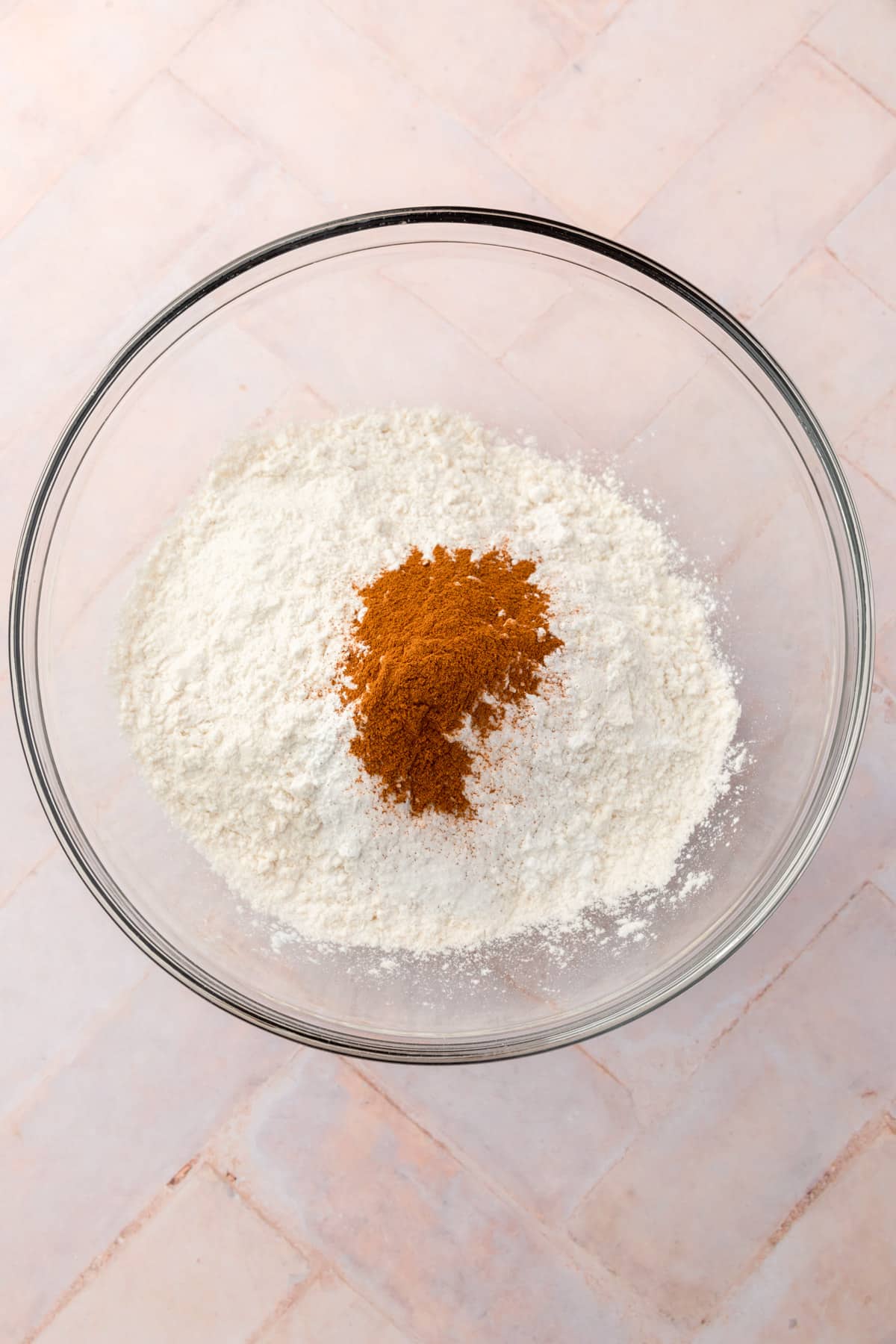 A glass mixing bowl with gluten-free flour, baking soda, baking powder, salt and cinnamon before mixing together.