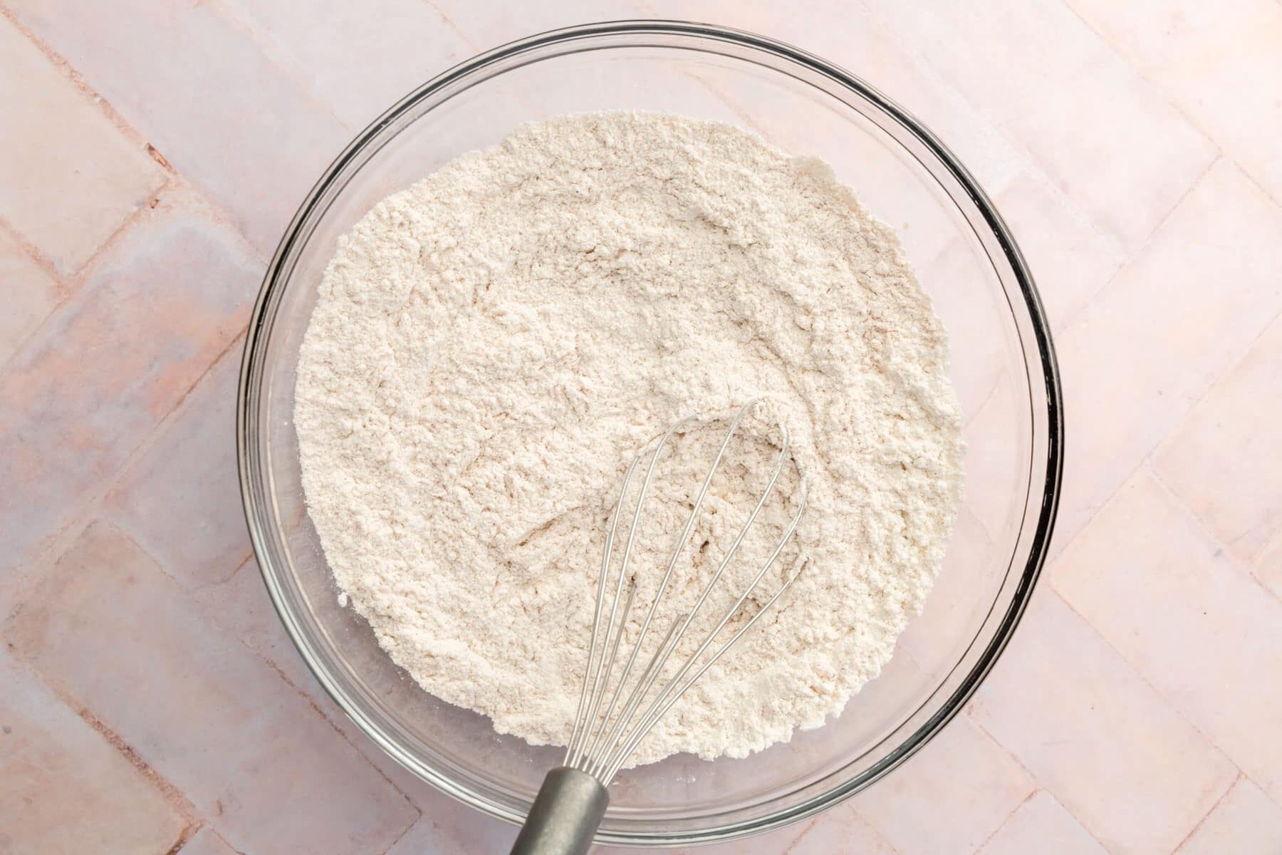 A glass mixing bowl with a gluten-free flour blend mixture with a whisk in it.